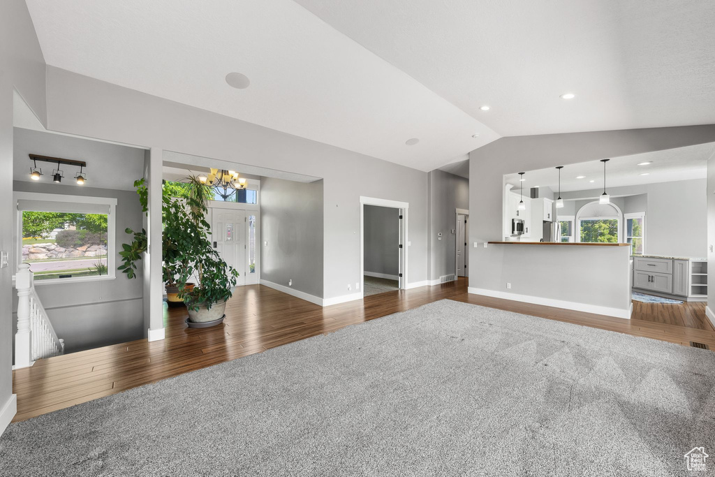 Living area featuring dark wood-type flooring, a chandelier, healthy amount of natural light, vaulted ceiling, and baseboards