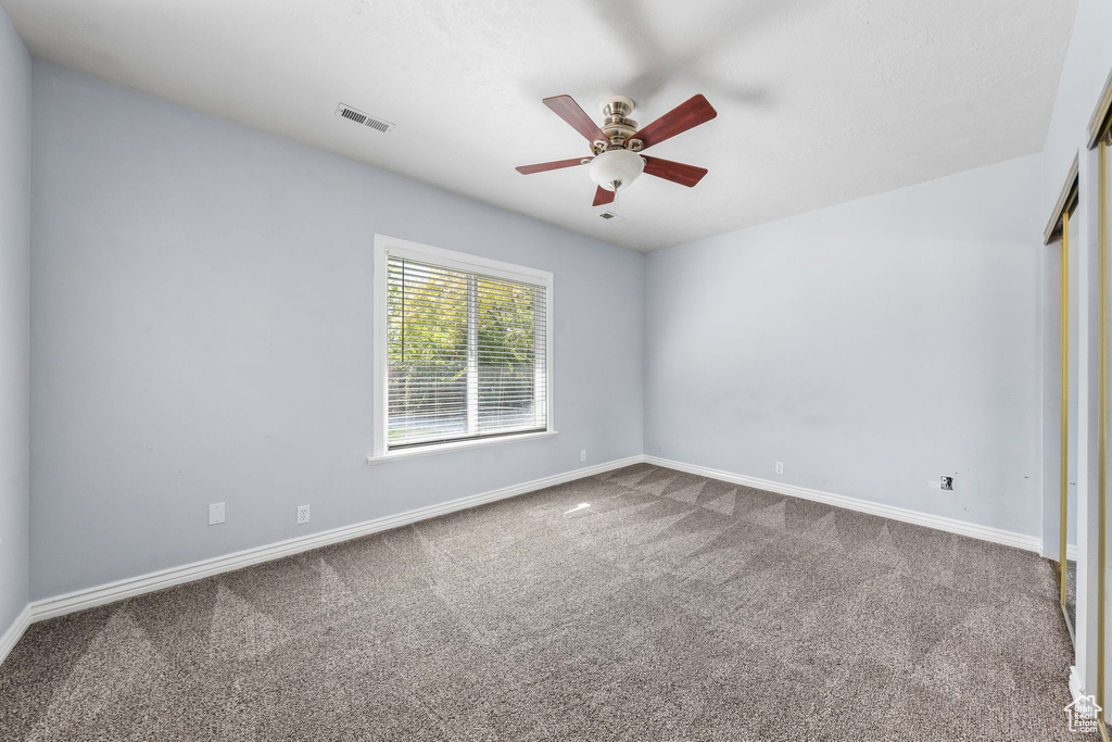 Carpeted spare room featuring ceiling fan and baseboards
