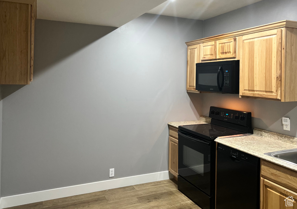 Kitchen featuring black appliances, light countertops, light wood-style flooring, baseboards, and light brown cabinets