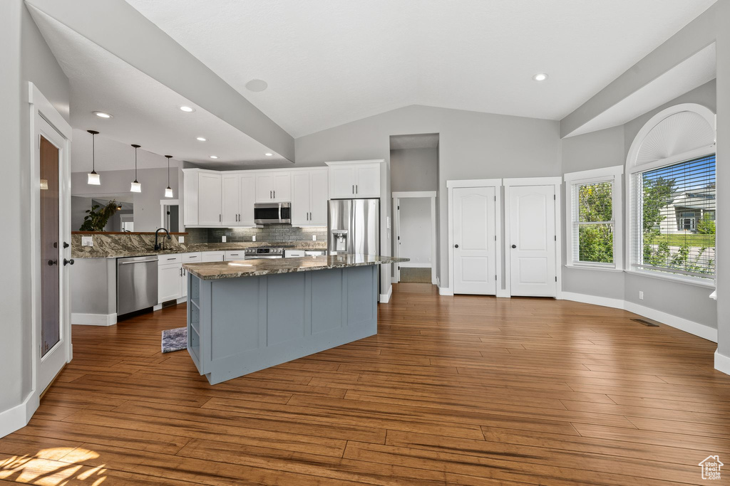 Kitchen with stainless steel appliances, a sink, lofted ceiling, white cabinets, and decorative backsplash