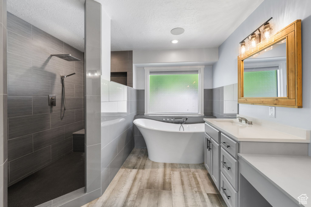 Full bath featuring walk in shower, a textured ceiling, vanity, a freestanding bath, and wood finished floors