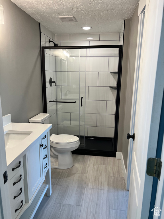 Full bath with a textured ceiling, a shower stall, vanity, and toilet