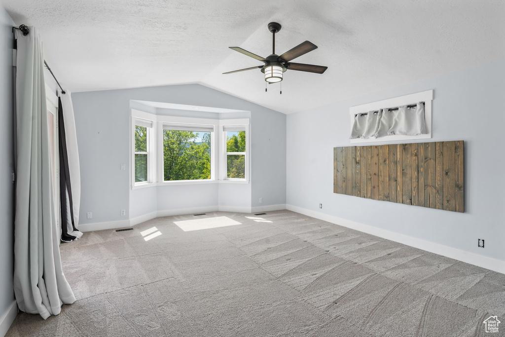 Unfurnished bedroom with vaulted ceiling, carpet, baseboards, ceiling fan, and a textured ceiling