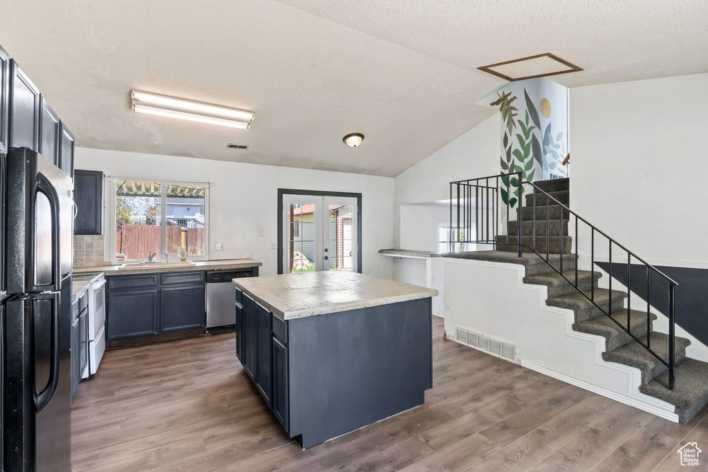 Kitchen featuring freestanding refrigerator, dishwasher, a kitchen island, wood finished floors, and a sink