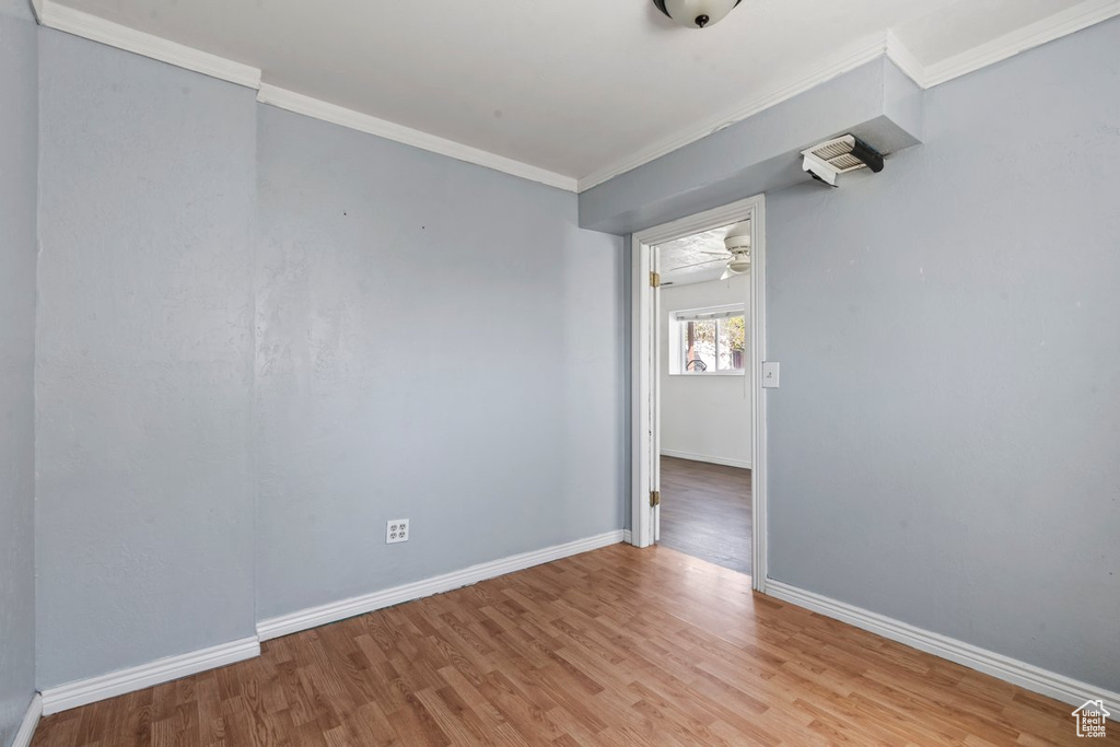 Empty room featuring light wood-type flooring, crown molding, and baseboards