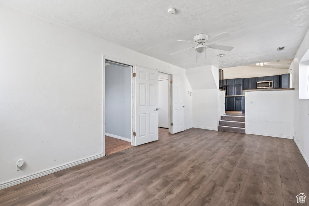 Unfurnished living room with ceiling fan, baseboards, dark wood finished floors, stairway, and a textured ceiling