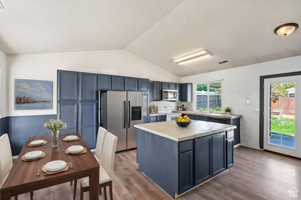 Kitchen with stainless steel appliances, light countertops, lofted ceiling, wood finished floors, and a kitchen island