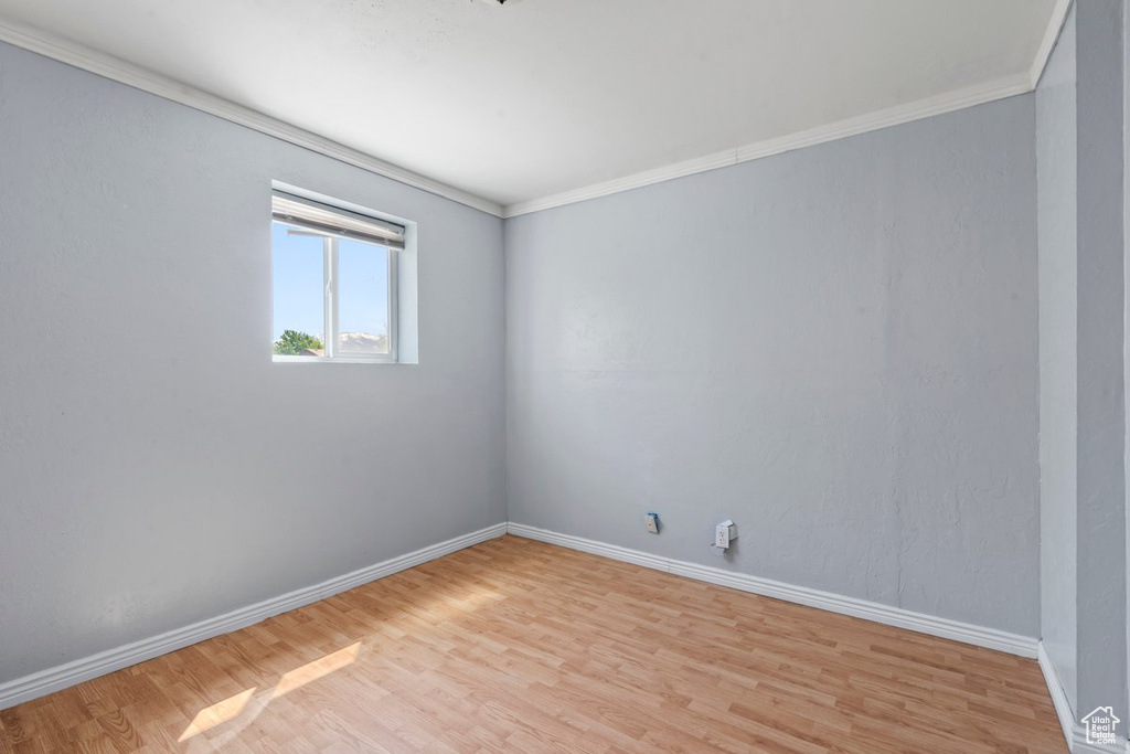 Empty room featuring light wood finished floors, baseboards, and crown molding