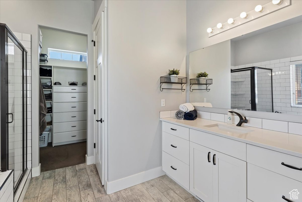 Full bath with a stall shower, wood finish floors, a walk in closet, vanity, and baseboards