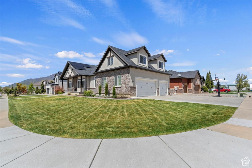 View of front of house featuring stone siding, an attached garage, a front yard, and a mountain view