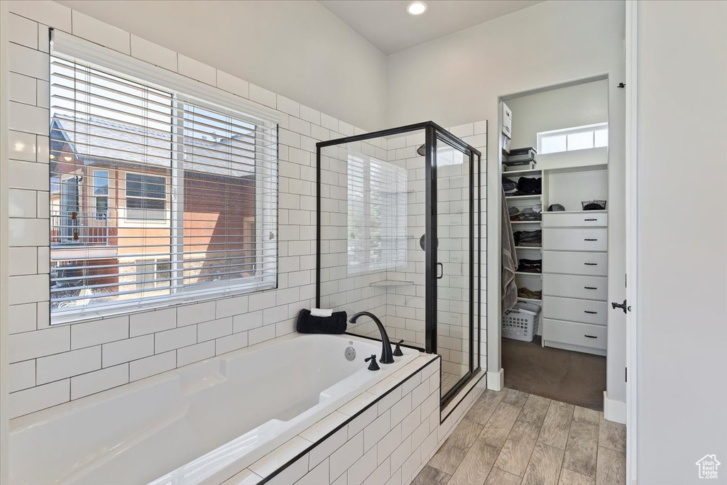 Full bath featuring a walk in closet, a stall shower, wood finished floors, a bath, and recessed lighting
