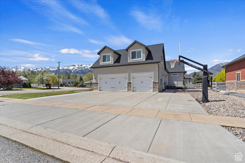View of side of property featuring driveway, a mountain view, stone siding, roof with shingles, and stucco siding