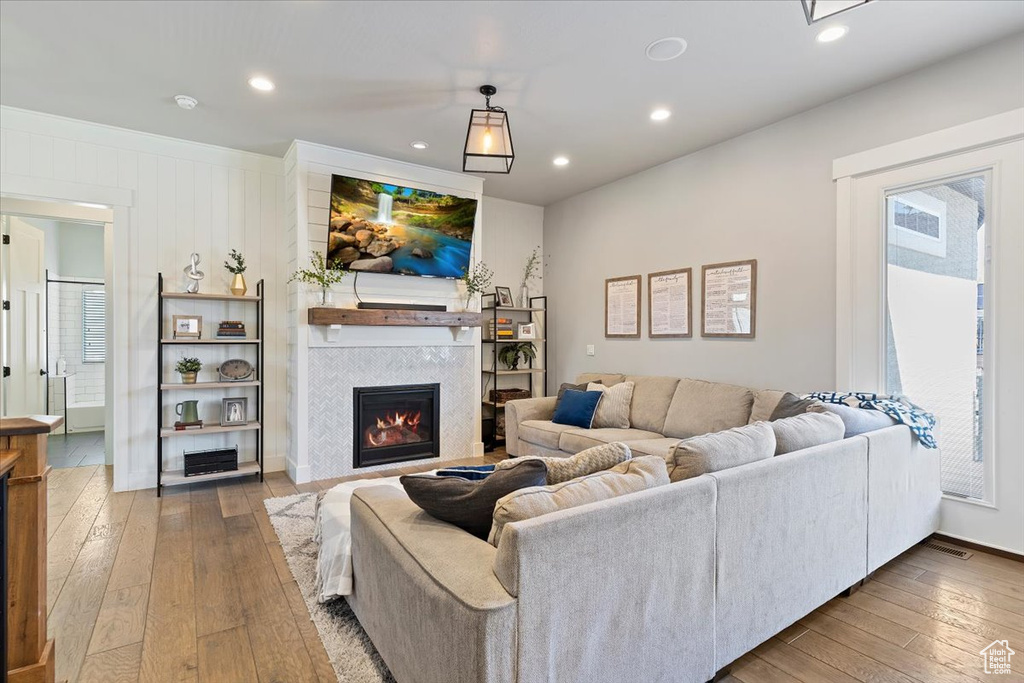 Living room with a warm lit fireplace, wood-type flooring, recessed lighting, and baseboards