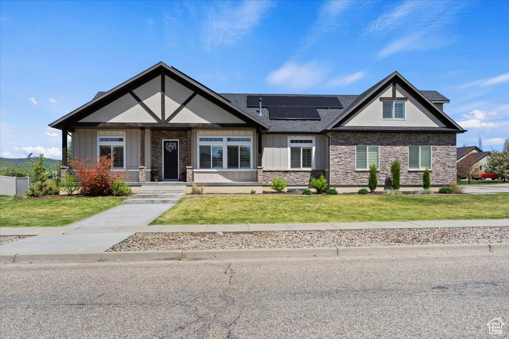 Craftsman house featuring board and batten siding, stone siding, roof mounted solar panels, a front yard, and covered porch