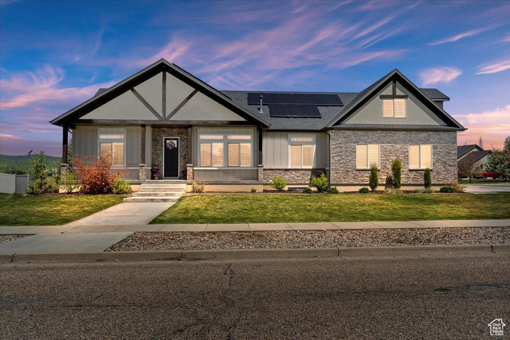 View of front facade featuring stone siding, roof mounted solar panels, a front yard, and board and batten siding