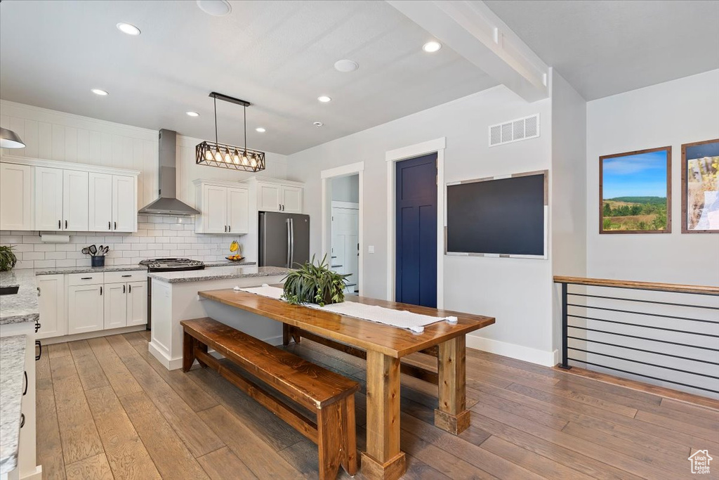 Kitchen with wall chimney range hood, freestanding refrigerator, light wood-style floors, white cabinets, and recessed lighting