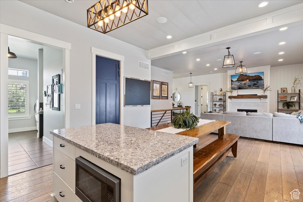 Kitchen featuring stainless steel microwave, light wood-style flooring, white cabinets, recessed lighting, and a kitchen island