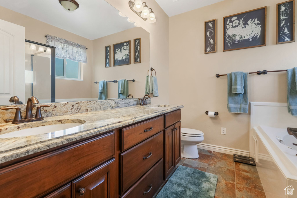 Bathroom featuring baseboards, toilet, double vanity, a bathtub, and stone finish floors