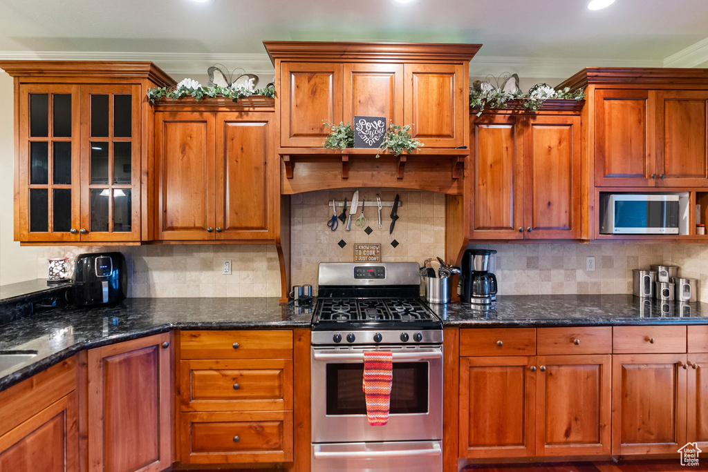 Kitchen featuring stainless steel appliances, ornamental molding, decorative backsplash, brown cabinetry, and glass insert cabinets