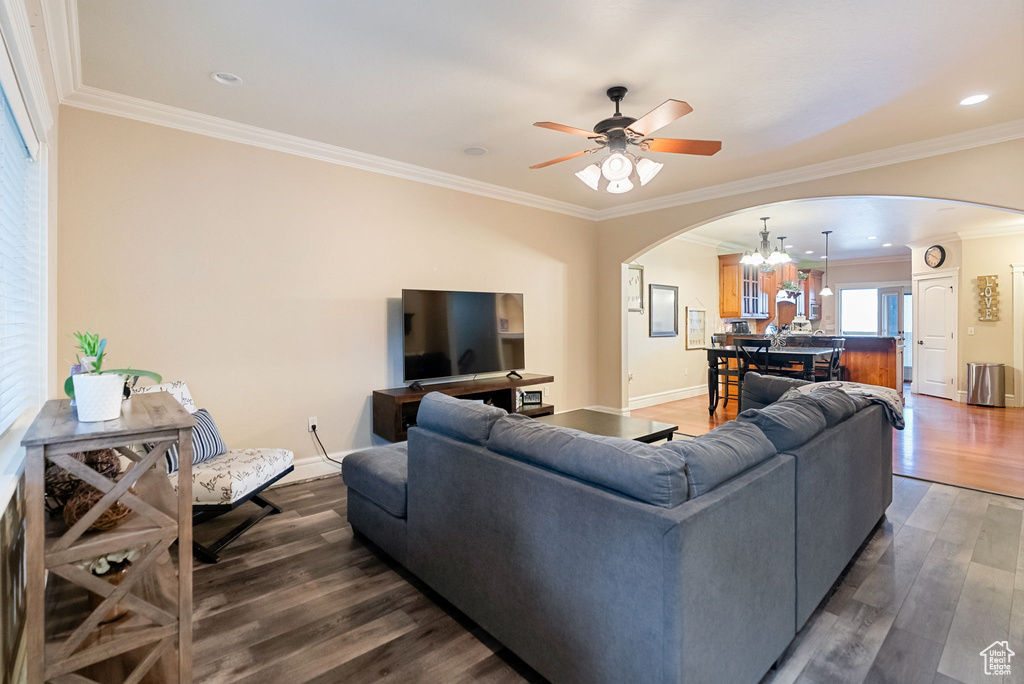 Living area featuring arched walkways, a chandelier, dark wood finished floors, ornamental molding, and a ceiling fan