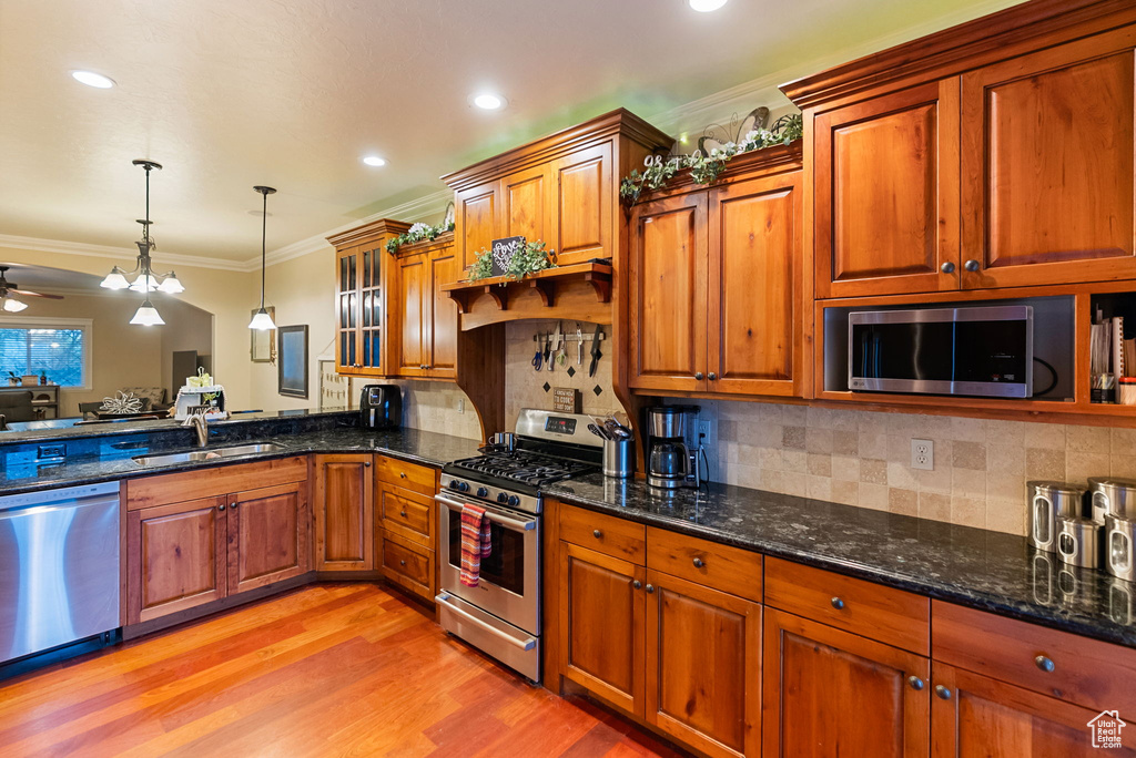 Kitchen with appliances with stainless steel finishes, brown cabinetry, a sink, hanging light fixtures, and ornamental molding