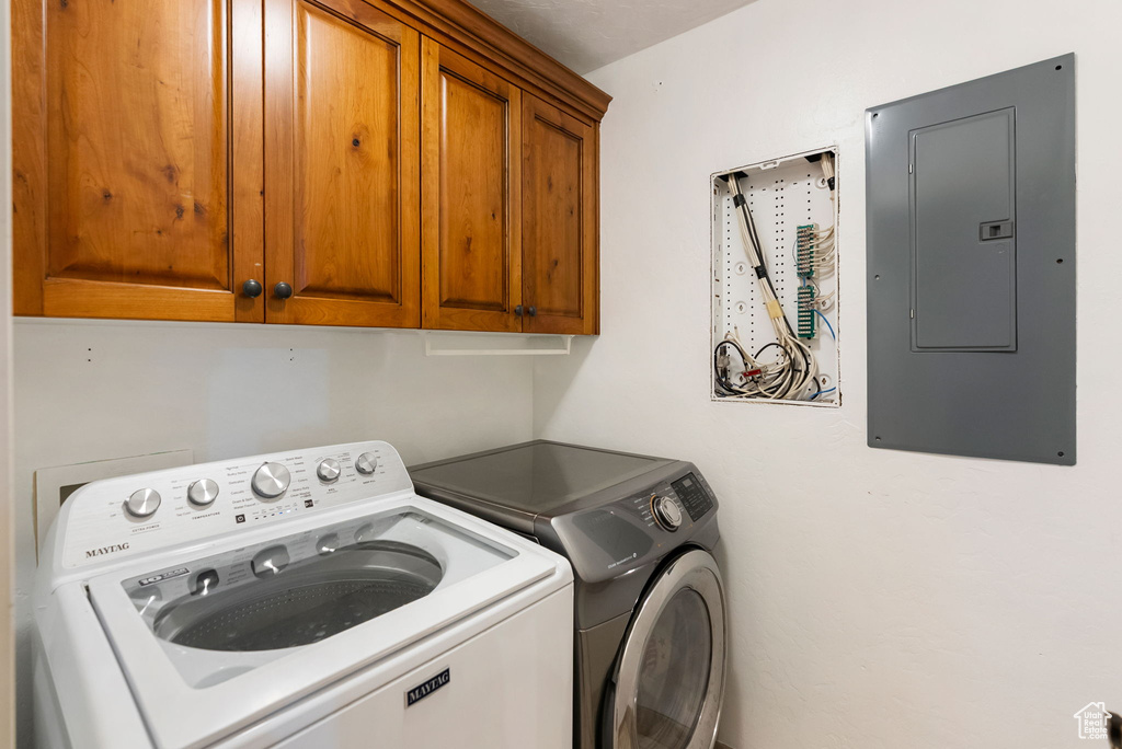 Clothes washing area featuring electric panel, cabinet space, and separate washer and dryer