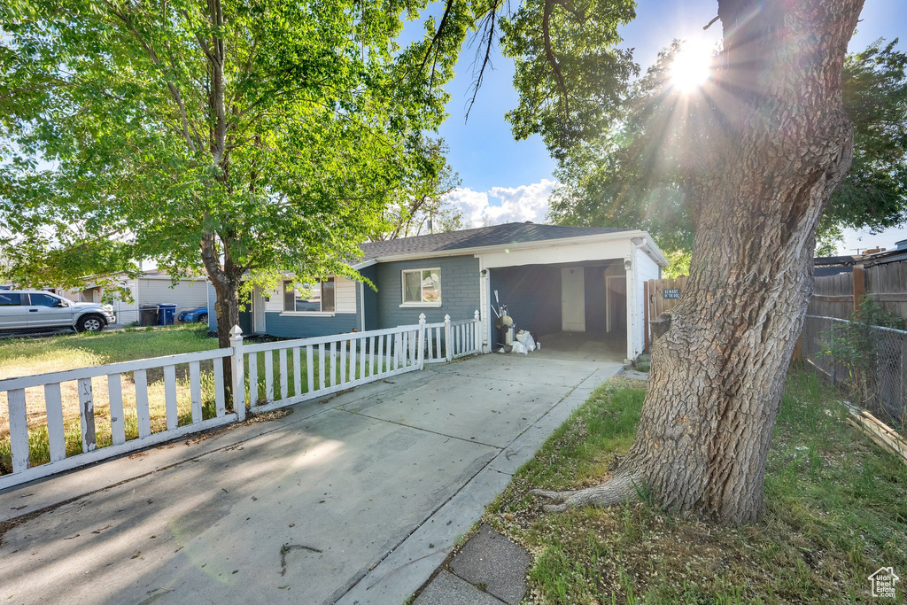 Garage with driveway, fence, and an attached carport