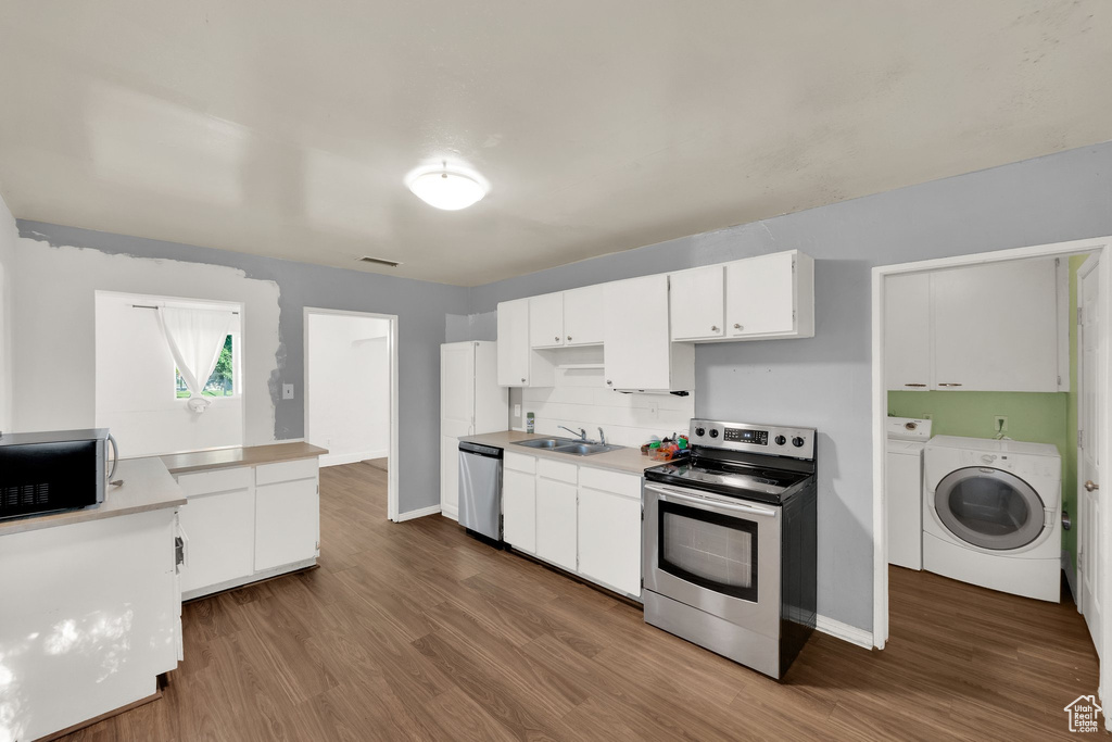 Kitchen with stainless steel appliances, a sink, washer and clothes dryer, and dark wood-style floors