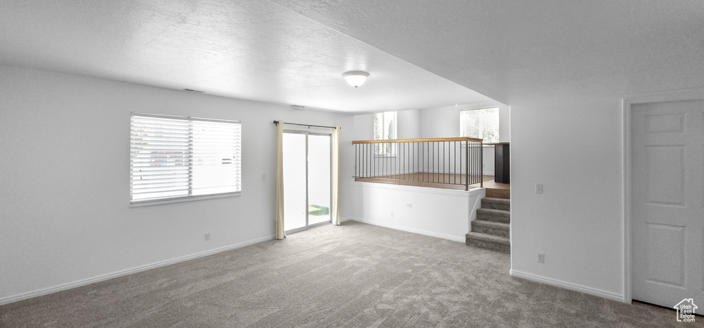 Unfurnished living room with carpet, baseboards, a textured ceiling, and stairway
