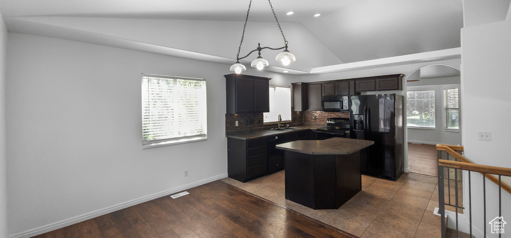 Kitchen featuring black appliances, a center island, a sink, dark countertops, and backsplash