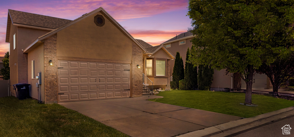 View of front of property with stucco siding, concrete driveway, an attached garage, a lawn, and stone siding