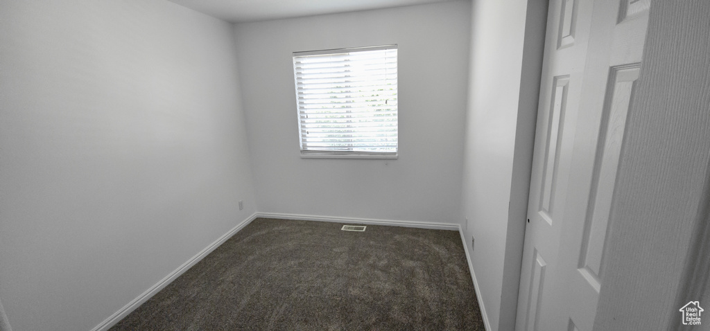 Spare room featuring dark carpet and baseboards
