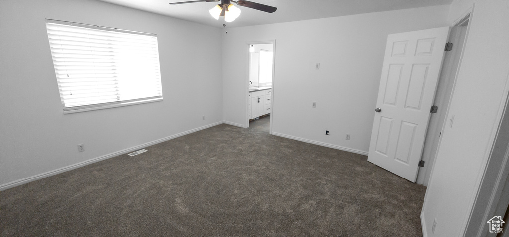 Unfurnished bedroom featuring dark colored carpet, connected bathroom, baseboards, and ceiling fan