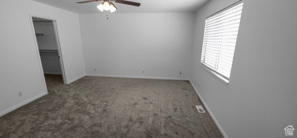 Unfurnished bedroom featuring a walk in closet, carpet flooring, baseboards, a closet, and a ceiling fan