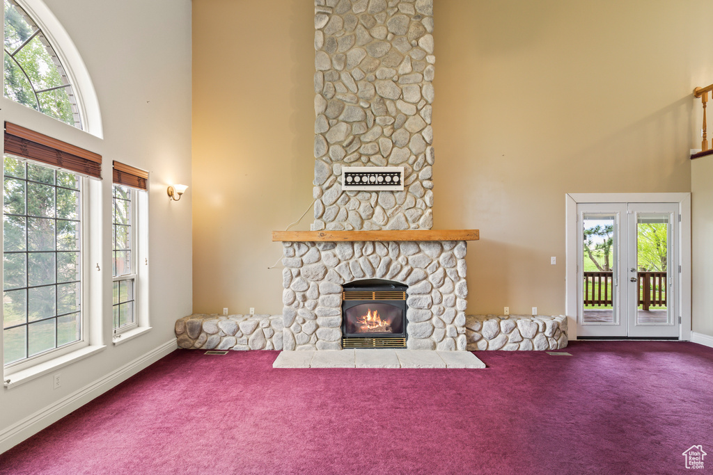 Unfurnished living room featuring a towering ceiling, carpet floors, a stone fireplace, french doors, and baseboards