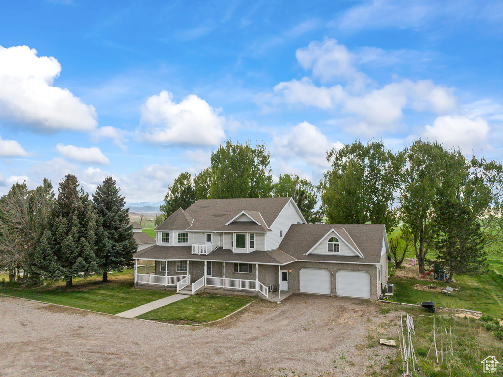 Multi unit property featuring a porch, a garage, dirt driveway, a front yard, and roof with shingles