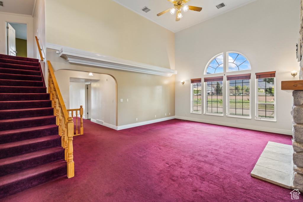 Unfurnished living room featuring carpet flooring, a high ceiling, ceiling fan, stairway, and baseboards