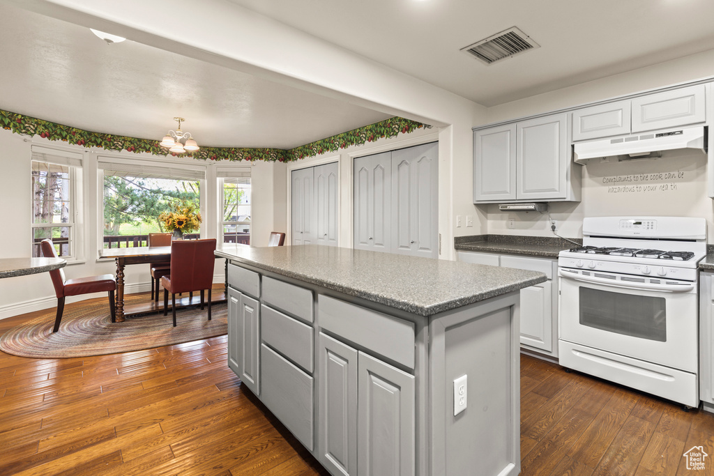 Kitchen featuring white gas stove, dark wood-style floors, under cabinet range hood, and a chandelier