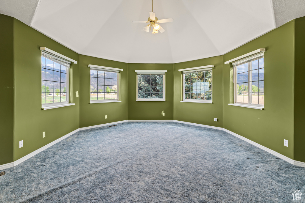 Carpeted empty room featuring lofted ceiling, a ceiling fan, and baseboards