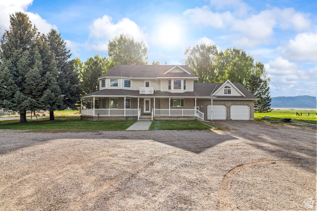 View of front of property featuring a porch, driveway, an attached garage, brick siding, and roof with shingles