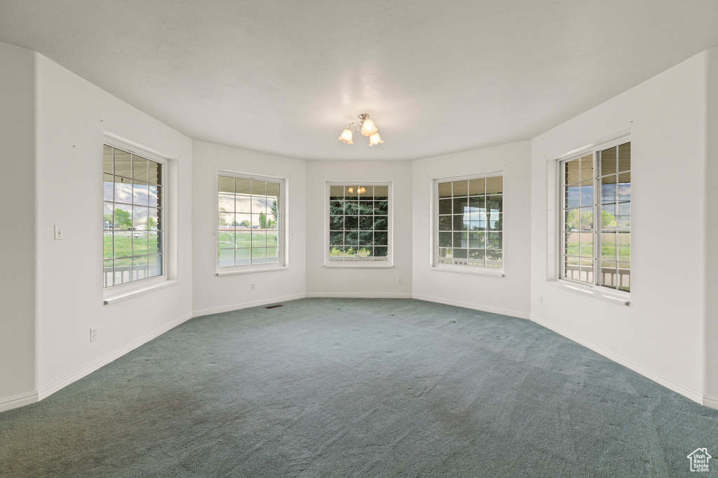 Empty room with carpet flooring, a chandelier, and baseboards