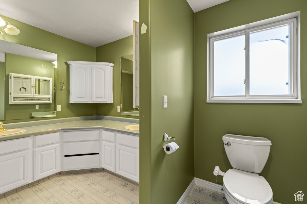 Bathroom with toilet, double vanity, and baseboards