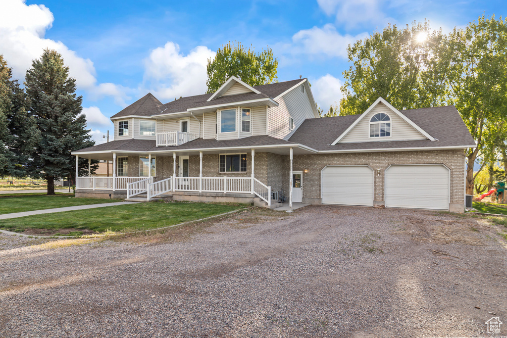 View of front of home featuring covered porch, dirt driveway, a garage, brick siding, and roof with shingles