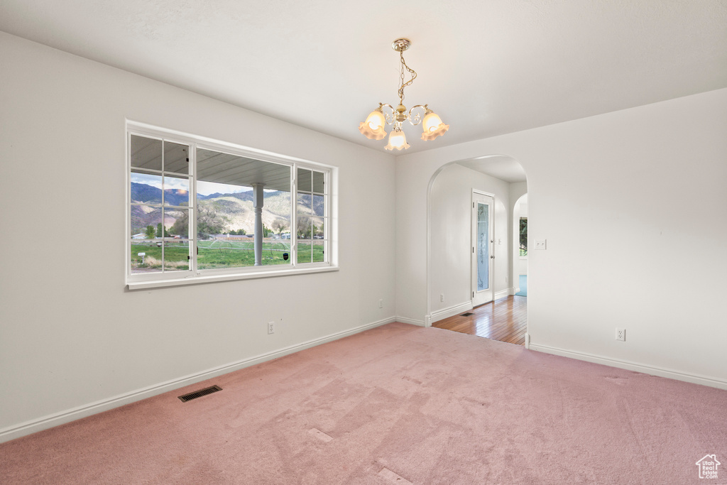 Carpeted spare room featuring arched walkways, baseboards, and a chandelier