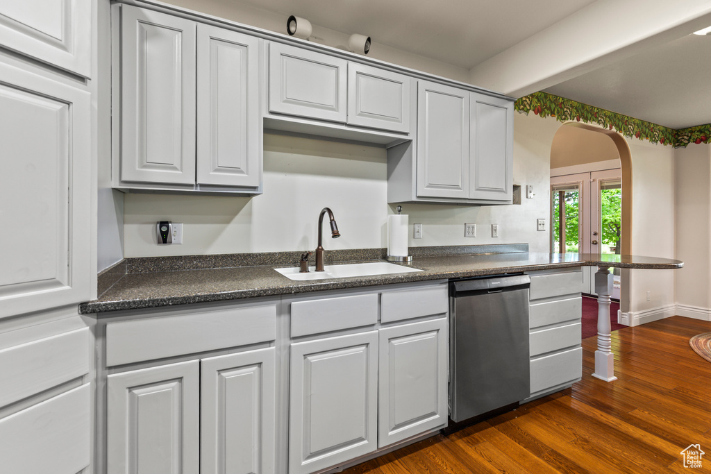 Kitchen with stainless steel dishwasher, a sink, dark countertops, arched walkways, and french doors