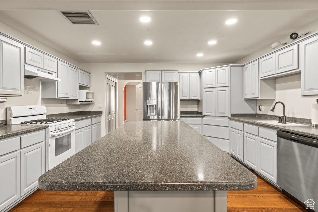 Kitchen with stainless steel appliances, under cabinet range hood, a sink, arched walkways, and recessed lighting