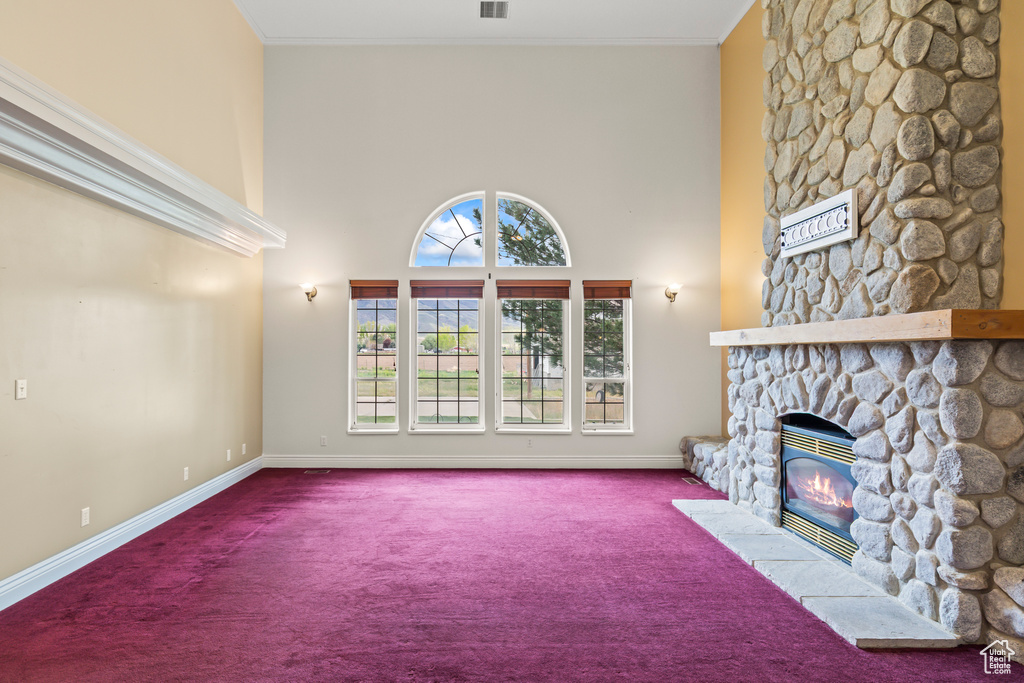 Unfurnished living room with carpet floors, baseboards, a stone fireplace, a high ceiling, and ornamental molding