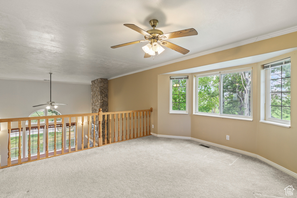 Empty room with ceiling fan, light colored carpet, baseboards, and crown molding