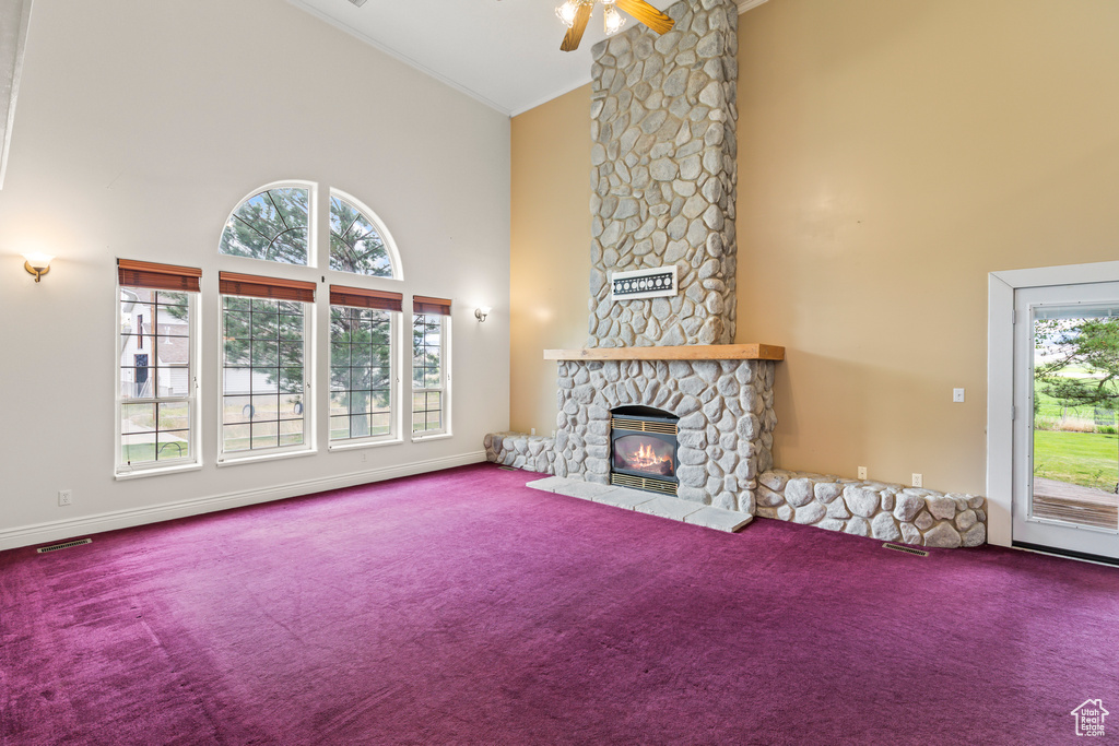 Unfurnished living room with carpet flooring, high vaulted ceiling, ornamental molding, a stone fireplace, and a ceiling fan