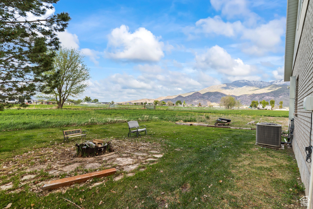 View of grassy yard featuring central air condition unit, a mountain view, and a rural view